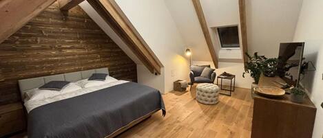 A bedroom with a bed, a chair, a small table, and a desk with a plant.