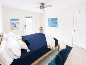 A bedroom with a bed, a ceiling fan, a door, and two wall-mounted paintings.
