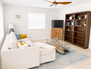 A living room with a sofa, a coffee table, a television on a wooden cabinet, and a bookshelf. - Riviera Blue - The Palm Beaches Retreat - Florida, 2BR/2BTH (West Palm Beach)