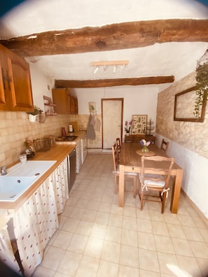 A kitchen with a wooden table and chairs, a sink, and a tiled floor. - House 'La Petite Maison de Village' with Private Terrace and Wi-Fi in the Heart of Provence (Vachères)