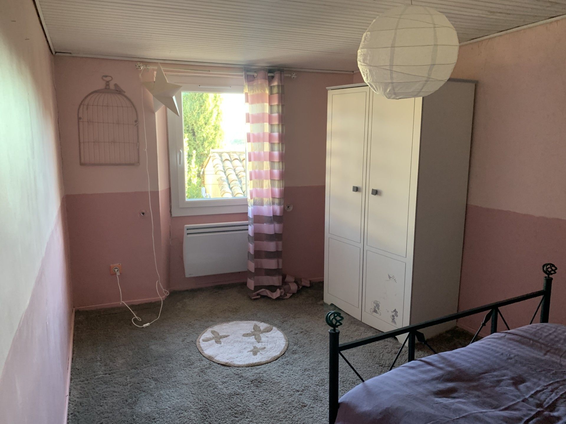 Ein Schlafzimmer mit Etagenbett, Kleiderschrank, Heizkörper, einem Fenster mit Vorhängen und einer Pendelleuchte.