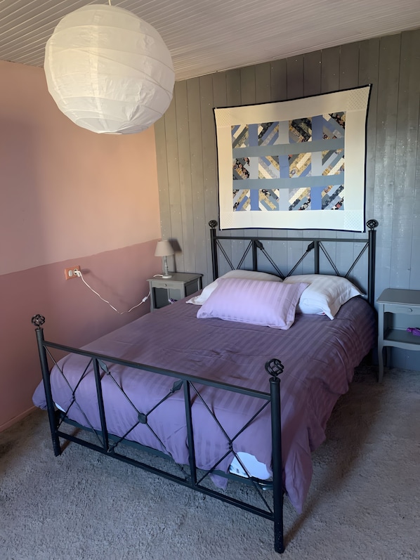 A bedroom with a bed, a nightstand, a lamp, a wall-mounted artwork, and a ceiling light fixture. - House 'La Petite Maison de Village' with Private Terrace and Wi-Fi in the Heart of Provence (Vachères)