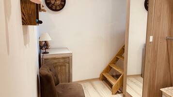 Ein Zimmer mit einem Holzstuhl, einem kleinen Schreibtisch mit Lampe, einer Uhr und einer Holzleiter.
