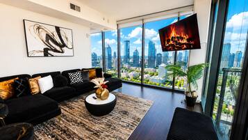 A modern living room with a black sofa, a round coffee table, and a large TV screen displaying a fire.