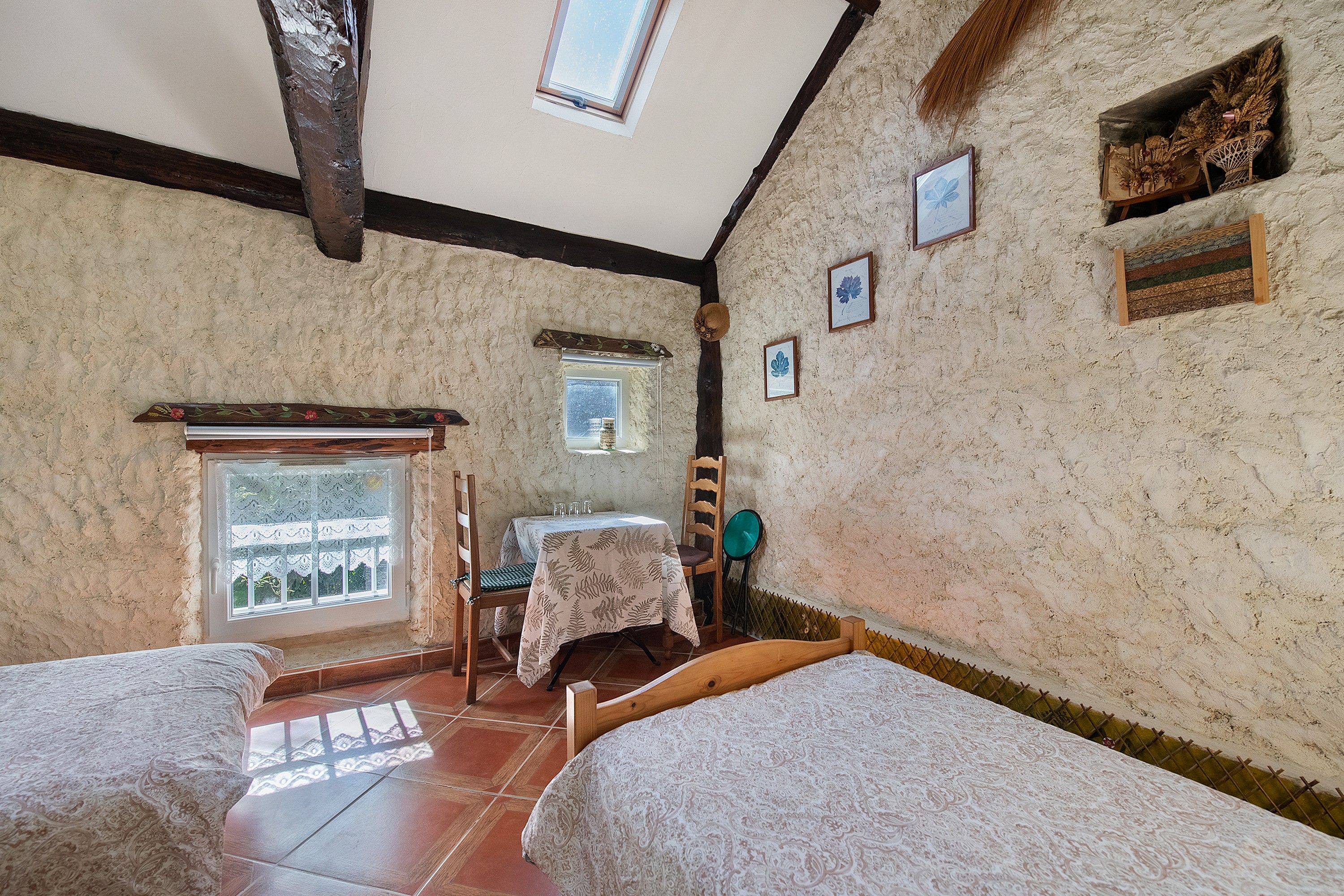 Una habitación con dos camas, una mesita, una silla y un ventanal con vistas.
