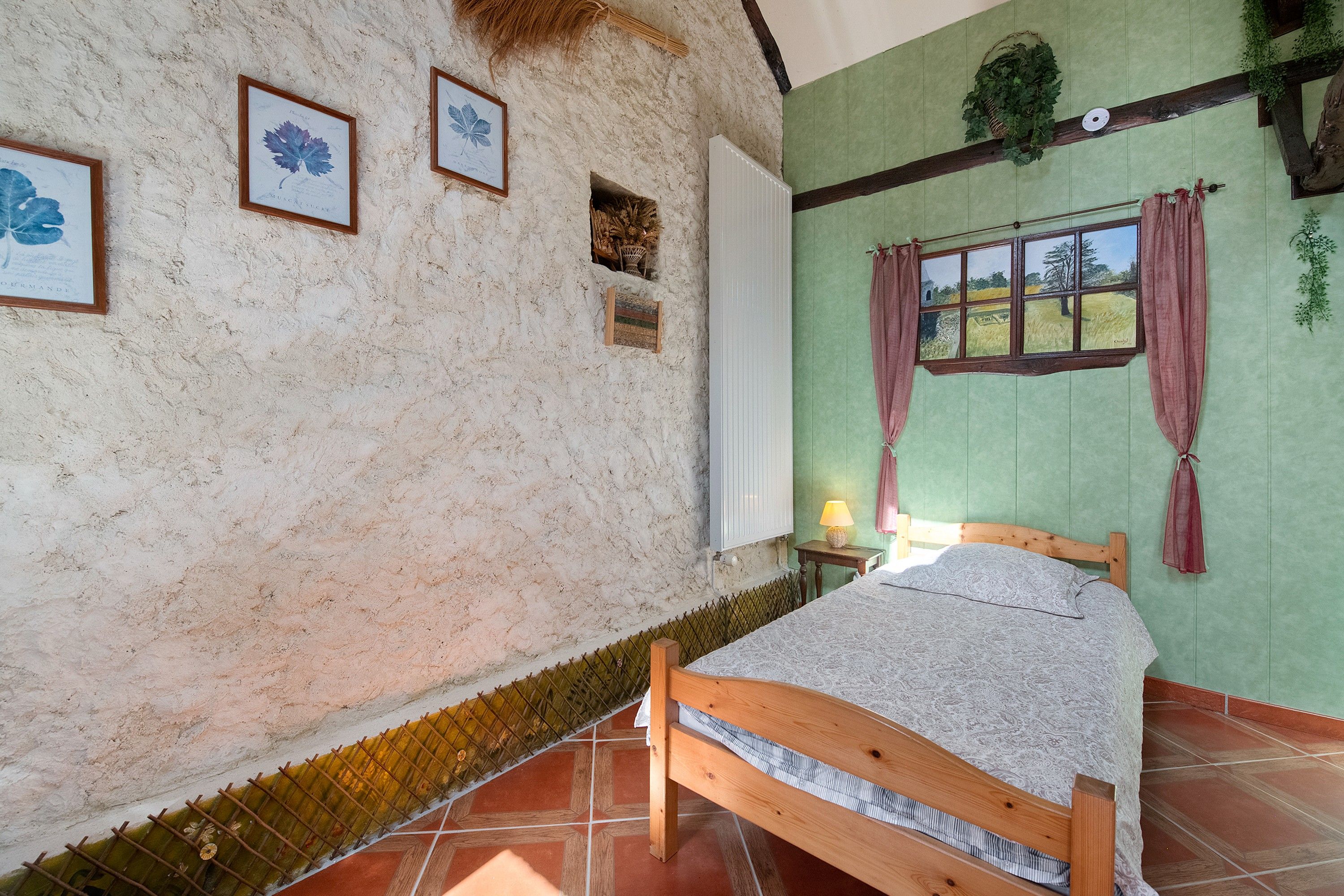 Ein Schlafzimmer mit einem Bett, einem Fenster mit Vorhängen, einer Lampe und gerahmten Pflanzenbildern an der Wand.