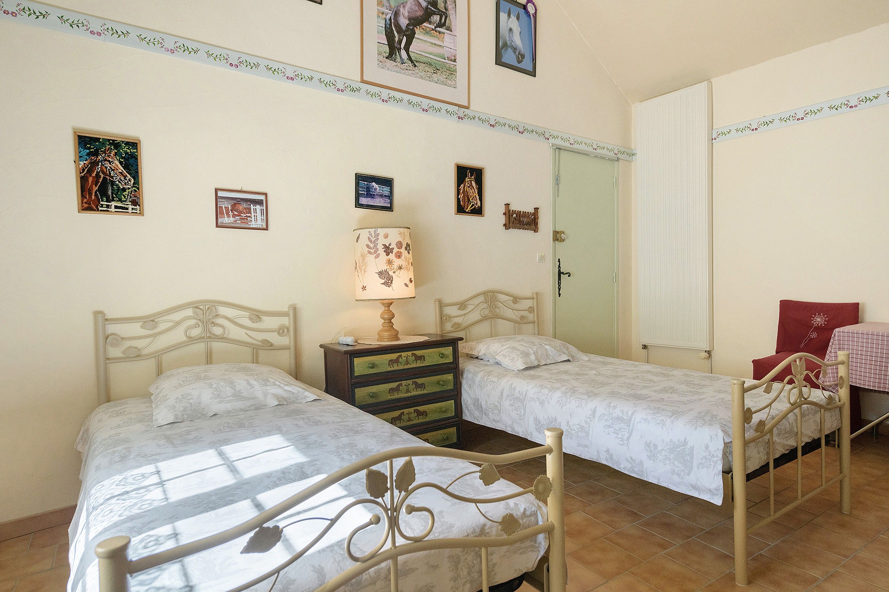Une chambre avec deux lits, une commode, une lampe et plusieurs tableaux encadrés accrochés au mur.