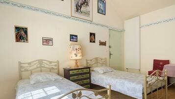 Une chambre avec deux lits, une commode, une lampe et plusieurs tableaux encadrés accrochés au mur.