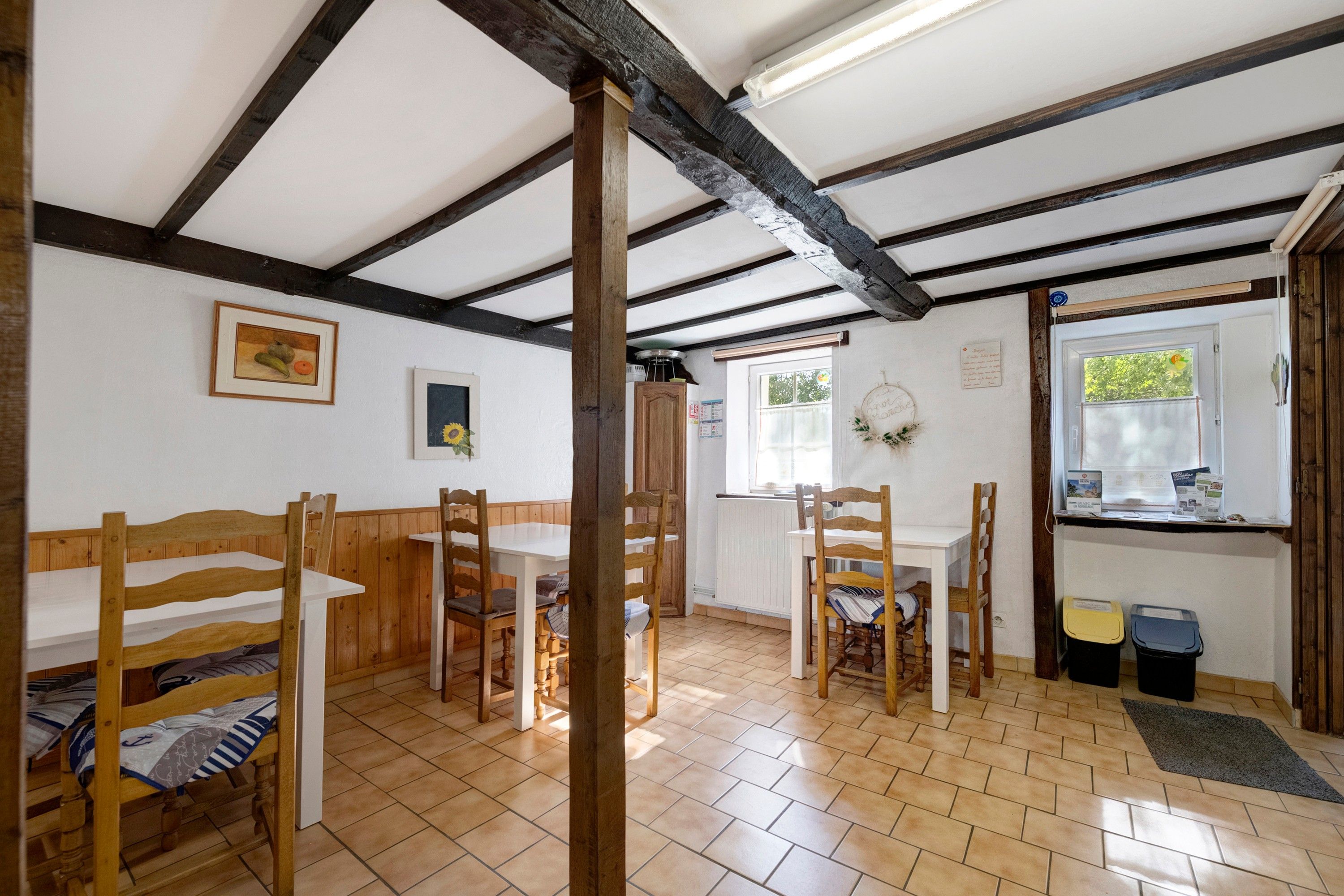 Une pièce avec un plafond en bois, une table à manger avec des chaises, un lit recouvert d’une couvre-lit à rayures et une fenêtre donnant sur un paysage verdoyant.