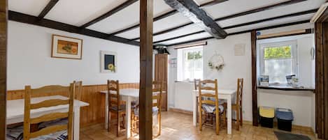 Een kamer met een houten plafond, een eettafel met stoelen, een bed met een gestreept dekbed en een raam met uitzicht op groen.
