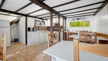 A rustic kitchen with exposed beams, a dining area with wooden chairs, and a tiled floor.