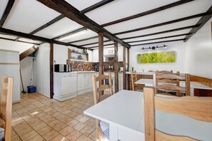 A rustic kitchen with exposed beams, a dining area with wooden chairs, and a tiled floor. - “La Cour Blanche L'Equestre” Room with Shared Terrace, Garden, and Wi-Fi (Castillon)