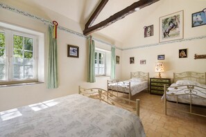 A bedroom with two beds, a window with curtains, and several framed pictures on the walls.