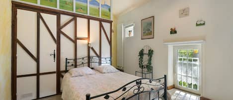 A bedroom with a bed, a window with a view, and a door with a painting.