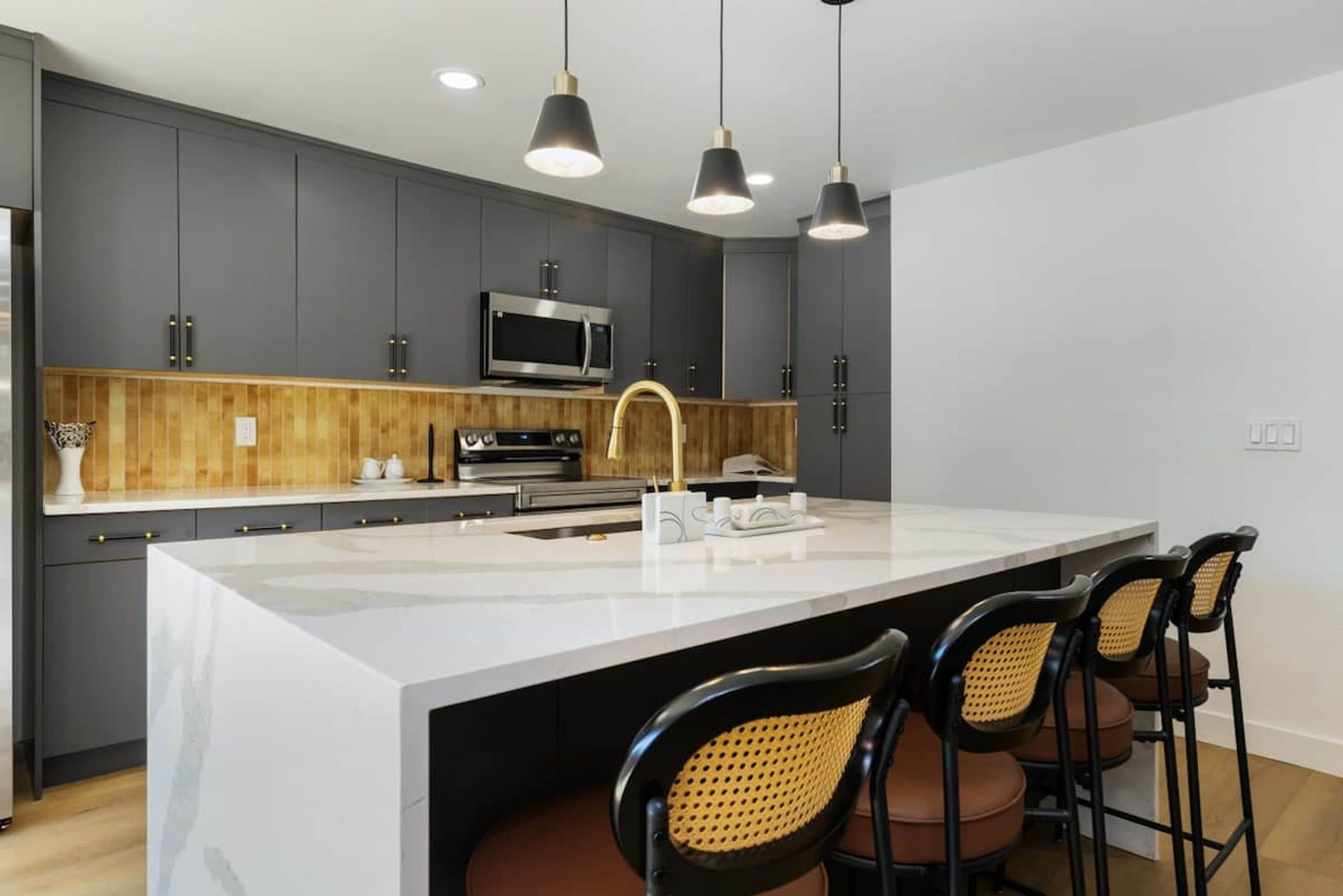 A modern kitchen with dark cabinets, a central island, a microwave, and bar stools.