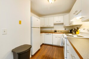 A compact kitchen with white cabinets, a dishwasher, a stove, and a trash bin. - Cozy 2BR Home in Lynnwood w  Backyard (Lynnwood)