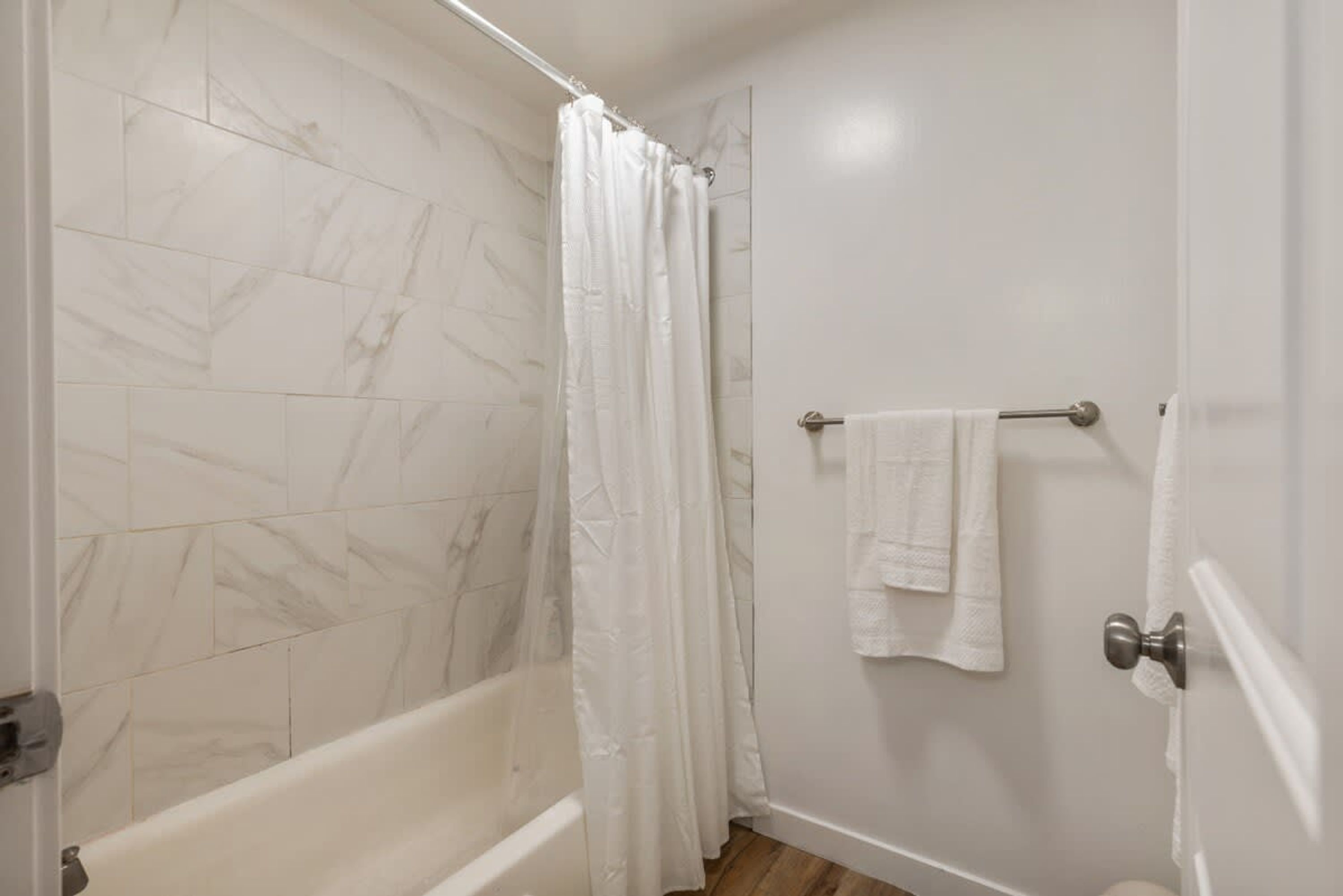 A bathroom with a bathtub, a shower curtain, and a towel rack with towels.