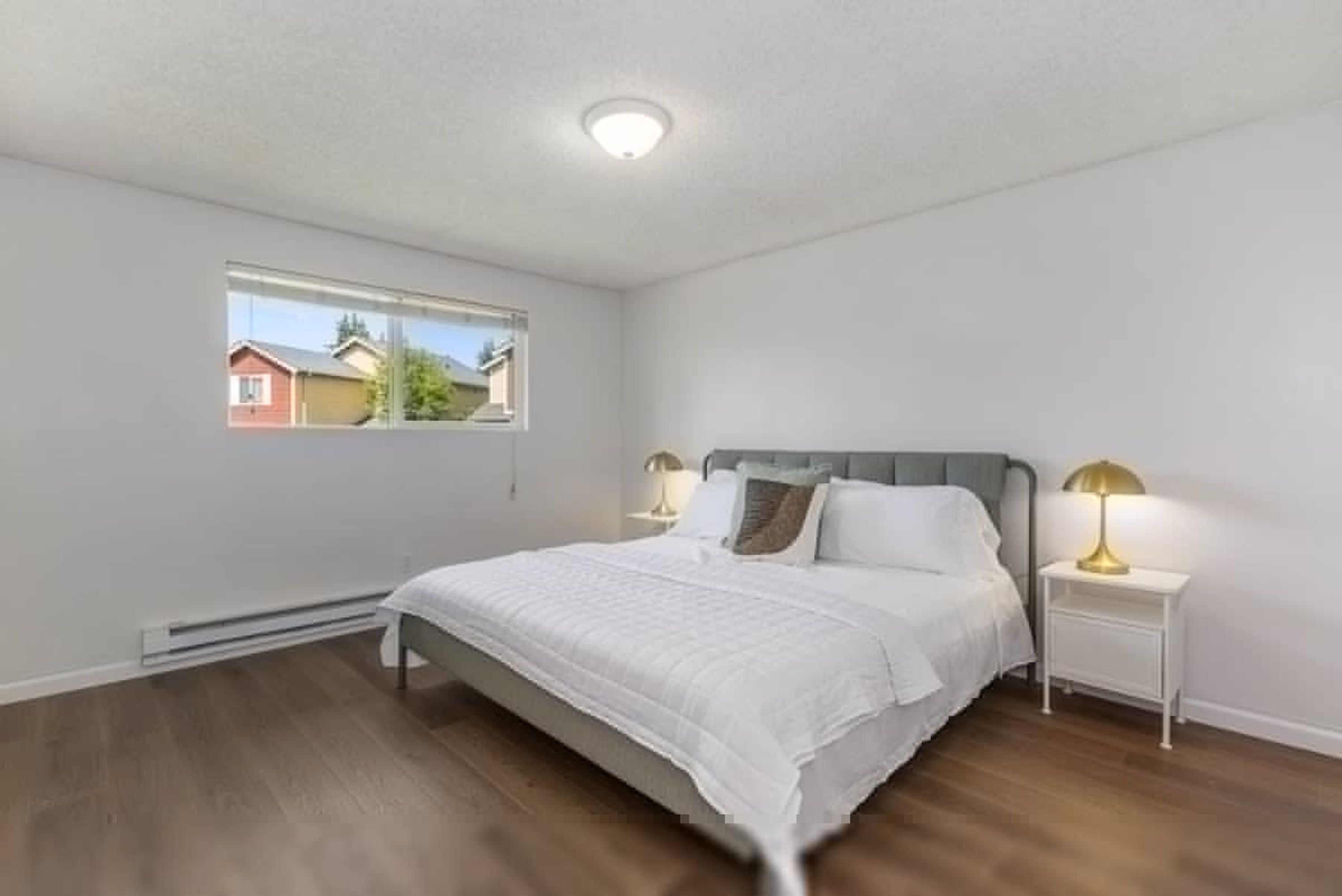Een slaapkamer met een bed, bedlampjes, een raam en een plafondlamp.