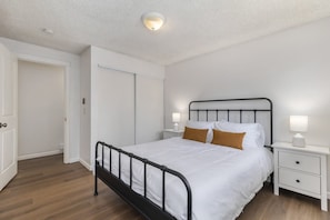 A bedroom with a single bed, white walls, a wooden floor, a white door, and a nightstand with a lamp. - Comfortable Townhouse in Ash Way Lynnwood (Lynnwood)