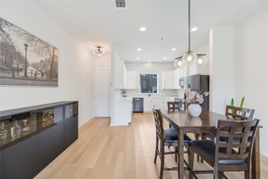 Eine moderne Küche mit weißen Schränken, ein Essbereich mit einem Holztisch und Stühlen sowie ein großes Bild an der Wand.