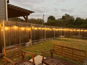 Ein Garten mit Holzzaun, Lichterketten und zwei Holzbänken.