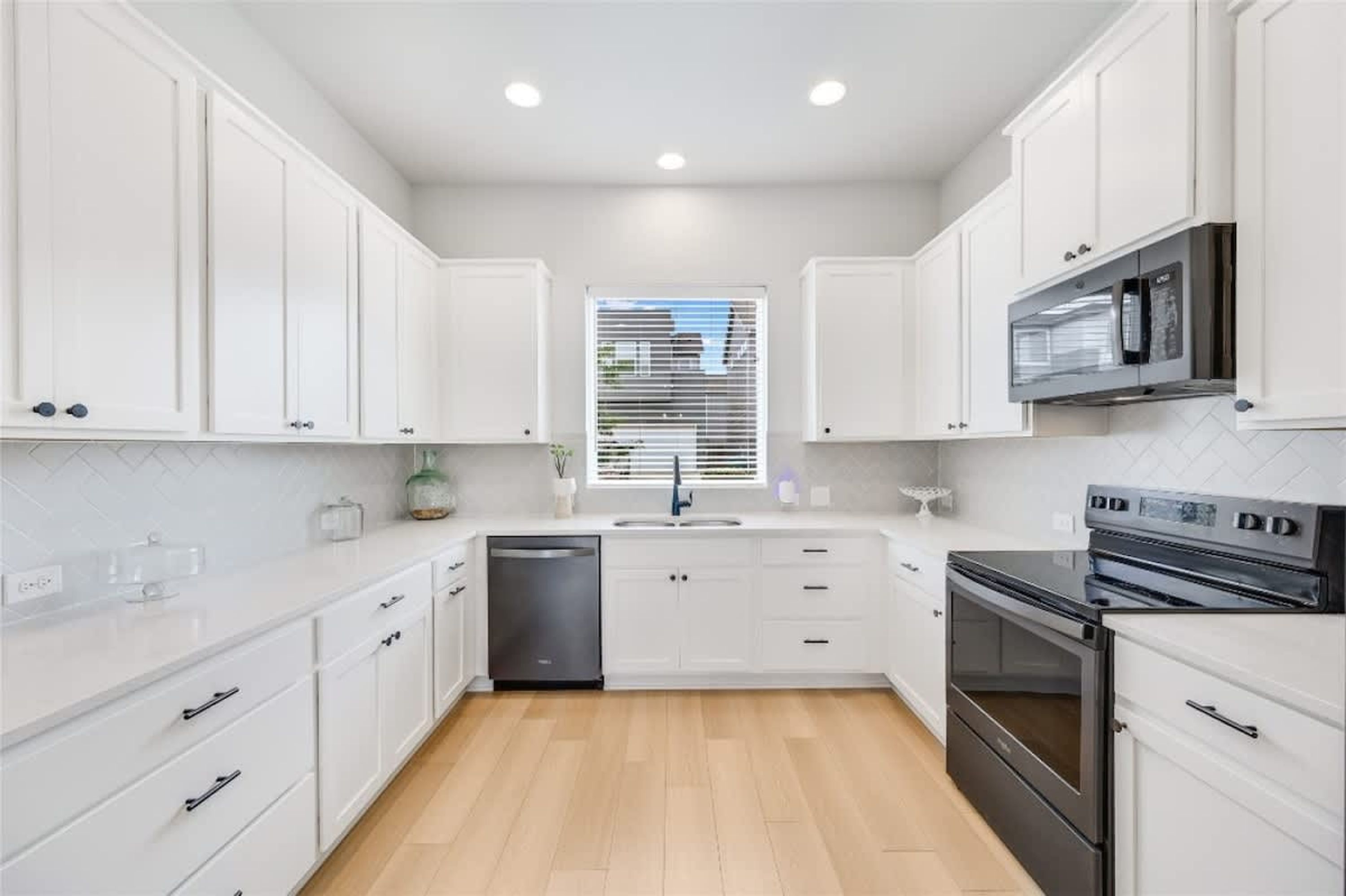 A modern kitchen with white cabinetry, a dishwasher, a stove, and a microwave.