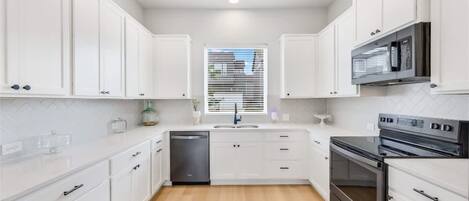 A modern kitchen with white cabinetry, a dishwasher, a stove, and a microwave.