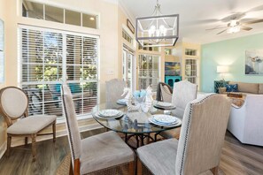 A dining area with a glass table, upholstered chairs, and a ceiling fan. - Golf Course View  Villa with Luxury 6 Seater Golf Cart  Steps to Beach   Pool   Tram just across from Entry (Miramar Beach)