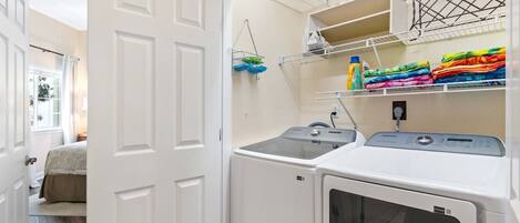 A laundry room with two washing machines, a drying rack, and shelves with folded clothes and laundry supplies.