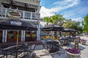 Outdoor seating with umbrellas, a building with a sign, and a palm tree. - Golf Course View  Villa with Luxury 6 Seater Golf Cart  Steps to Beach   Pool   Tram just across from Entry (Miramar Beach)