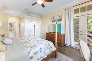 Ein Schlafzimmer mit einem Bett, einer Kommode, einem Fernseher und einer Tür, die auf einen Balkon führt.