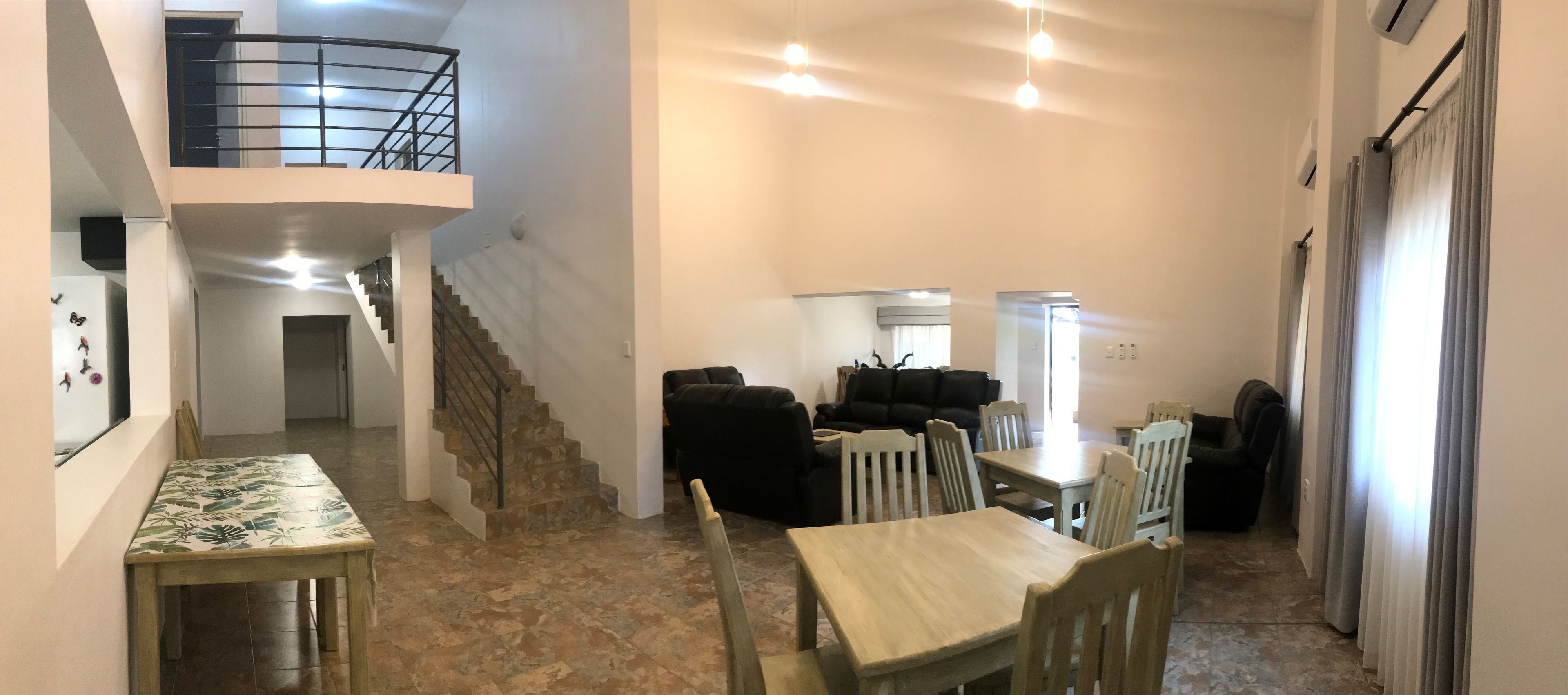 A spacious living area with a dining table, chairs, a sofa, and a staircase leading to an upper level.