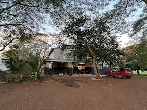 A house with a covered porch, a red car parked in front, and a tree in the foreground.