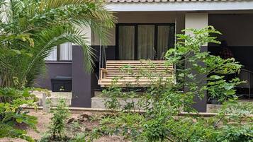 A wooden bench in a garden area with plants and a building in the background.