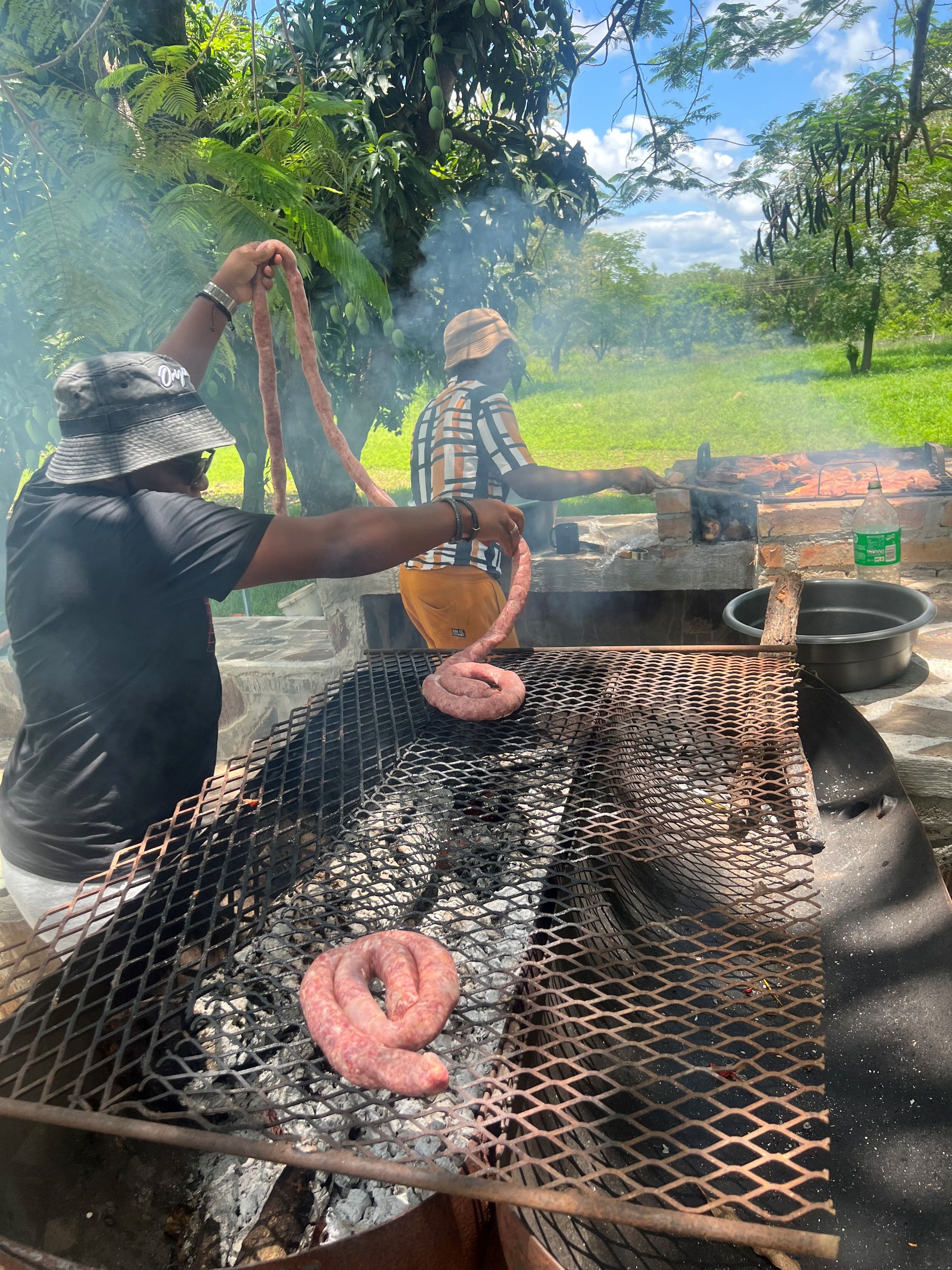 A person grilling sausages outdoors with a grill and cooking utensils visible.