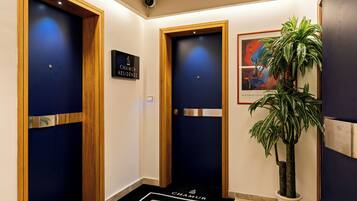 Un vestíbulo de hotel con dos puertas, un letrero sobre cada una, una planta en maceta y una obra de arte enmarcada en la pared.
