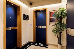 Un vestíbul d'hotel amb dues portes, un senyal sobre cada porta, una planta en test i una obra d'art emmarcada a la paret.