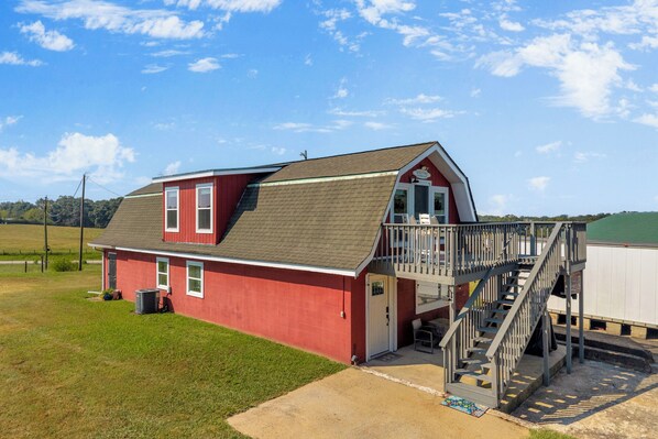 A red barn with a balcony and a staircase leading to a covered area.