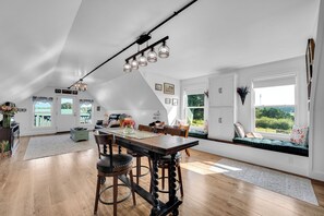 A spacious kitchen with a central island, wooden flooring, and a view of the outdoors through large windows.