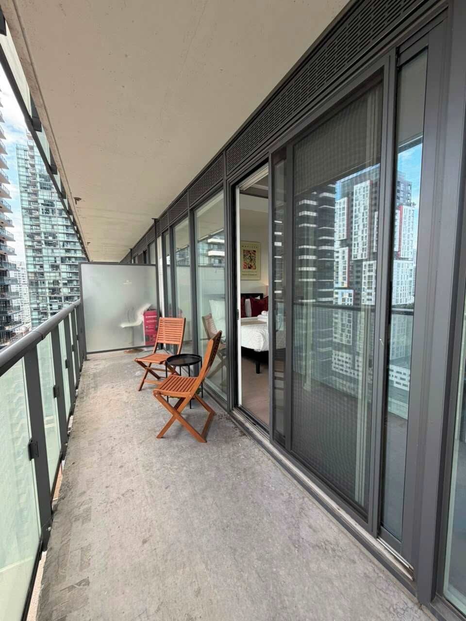 A balcony with a view of a cityscape, a bed, and two wooden chairs.