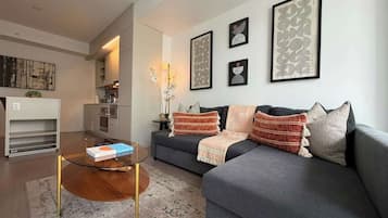 Una sala de estar moderna con un sofá gris, una mesa de centro de vidrio y una estantería.