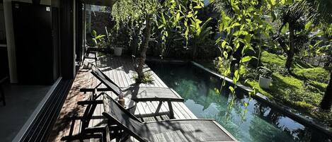 Terraza de madera con sillones de descanso con vista a una piscina cristalina, rodeada de exuberante vegetación.