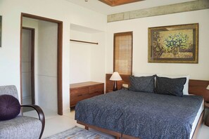 Un dormitorio con cama, una silla, una mesita de noche, una lámpara, un cuadro y una puerta.