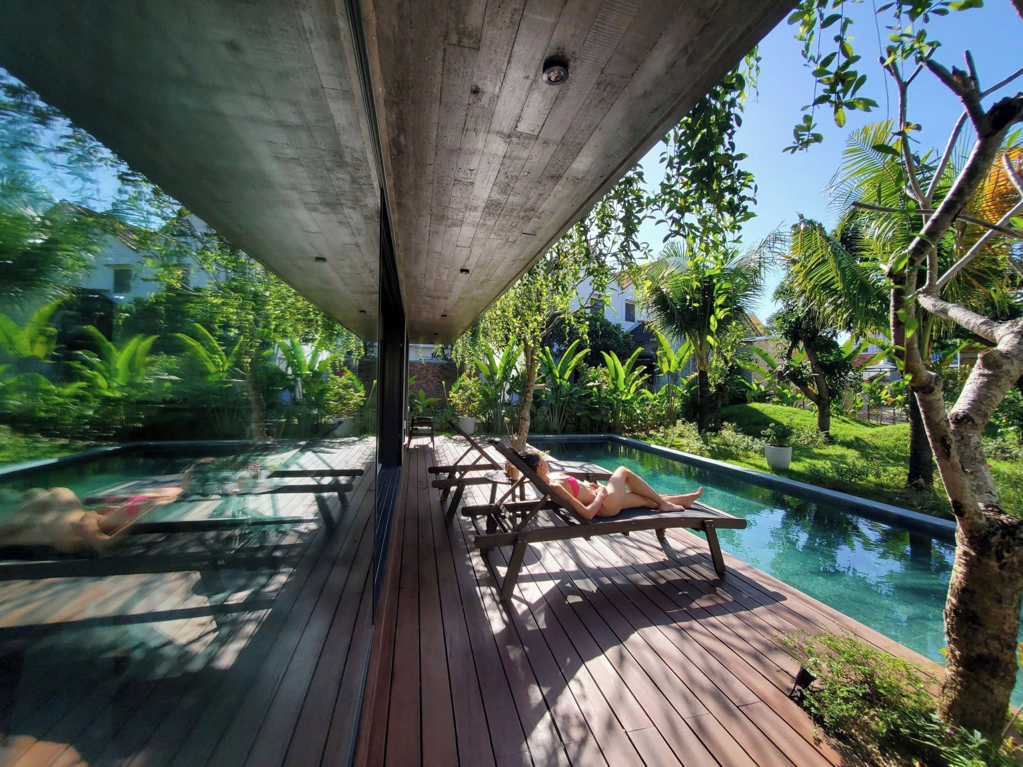 A wooden deck with lounge chairs overlooking a swimming pool, surrounded by lush greenery.