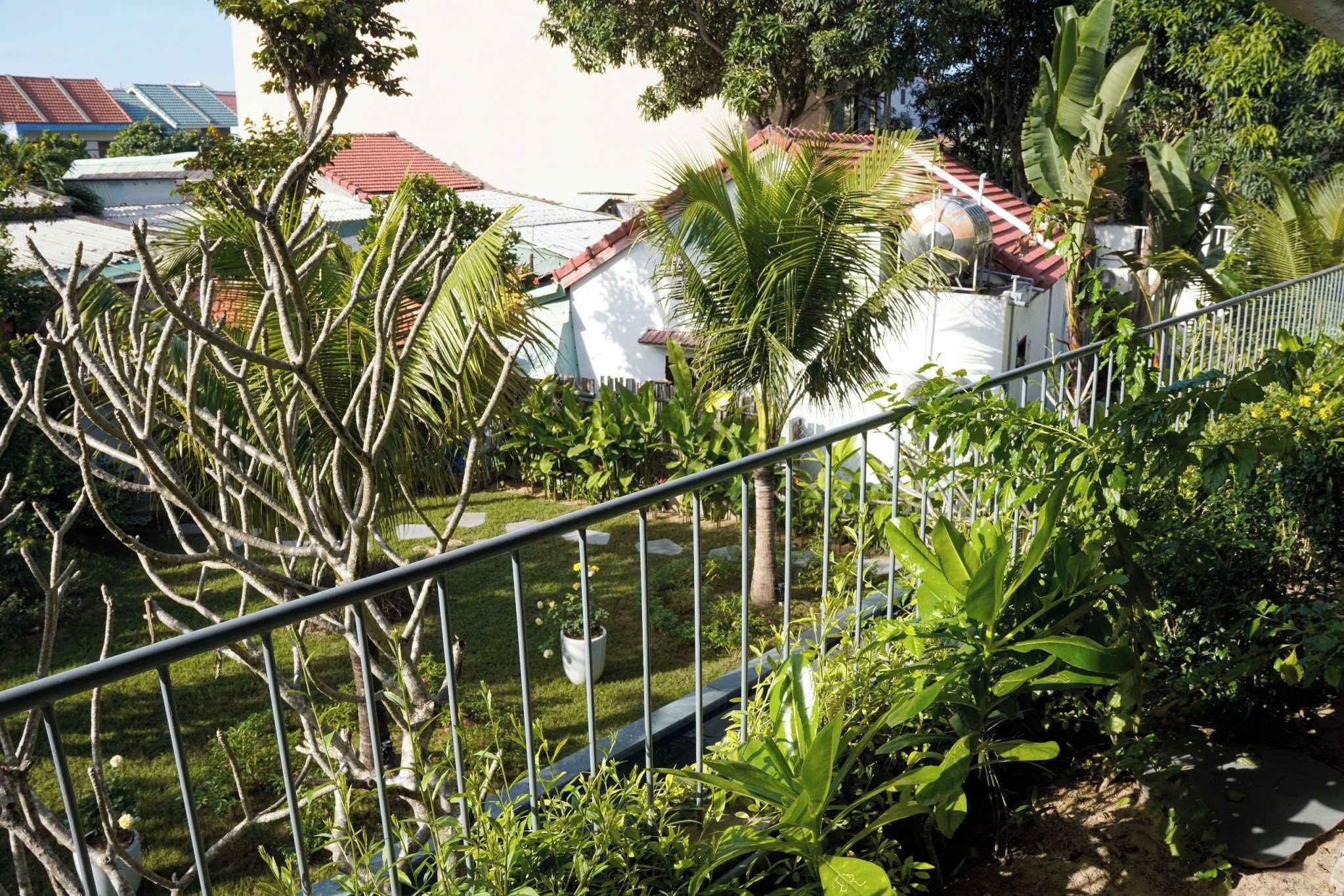 Un quartier résidentiel caractérisé par un bâtiment blanc, des toits recouverts de tuiles rouges et une végétation luxuriante comprenant des palmiers et diverses plantes.