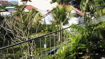Un quartier résidentiel caractérisé par un bâtiment blanc, des toits recouverts de tuiles rouges et une végétation luxuriante comprenant des palmiers et diverses plantes.