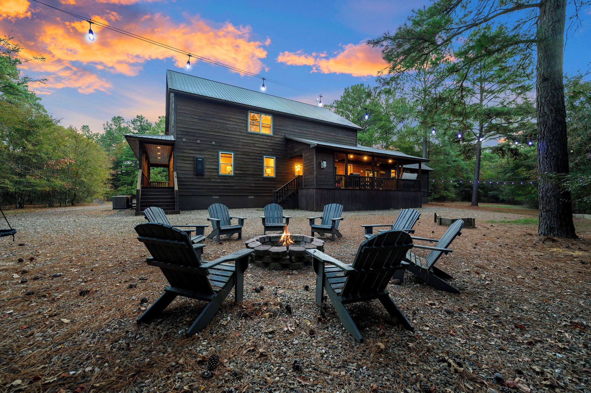 A rustic cabin with a fire pit and Adirondack chairs in the foreground, surrounded by trees.