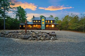 A two-story lodge with a stone foundation, wooden exterior, and a porch with a railing. - 4 King Bedrooms | Hot Tub | Game Room (Broken Bow)