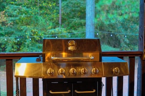 Ein Grill mit vier Brennern und einem Thermometer auf einer Holzterrasse mit Blick auf Bäume.