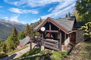 A mountain cabin with a wooden deck and a stone wall.
